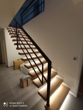 Nowoczesne schody w stylu loftowym o drewnianych, podświetlanych stopniach i czarnej balustradzie